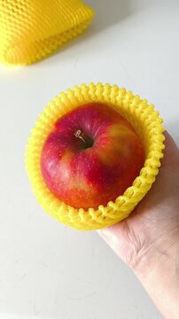 Close-up of an apple in a yellow foam net in your hand. Packaging for transportation, delivery of vegetables.