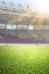 Naklejka premium Close-up of lush green grass on a professional soccer field with a blurred stadium and bright sunlight in the background. Ideal for sport-themed designs
