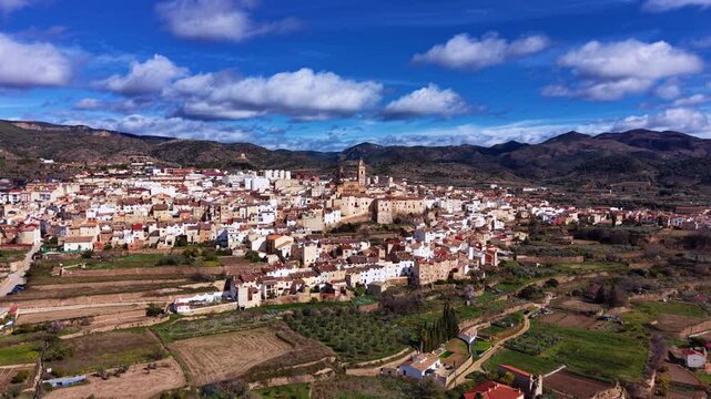 Chelva historic town in Valencia province, Spain, with church tower rising above white houses, surrounded by terraced fields and mountain hills