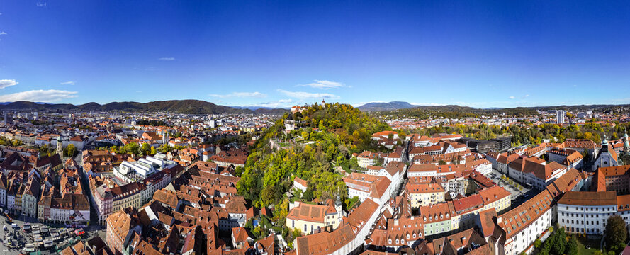 Aerial view of the vibrant red rooftops cascading towards the verdant Schlossberg hill crowned by the clock tower, a timeless landmark, Graz, Styria, Austria.