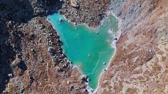 Spiral drone shot of turquoise Chiaretto Lake surrounded by mountains in Monviso Alps Italy.