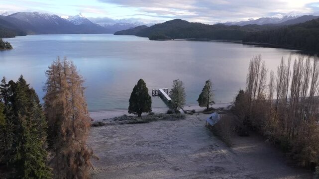 Aerial approach to snowy pier on Lake Espejo, Patagonia, serene winter landscape.