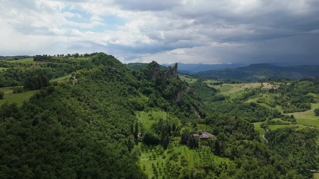 Zoom in aerial highlighting Rocca Malatina rock formations rising from green hills in Italy.