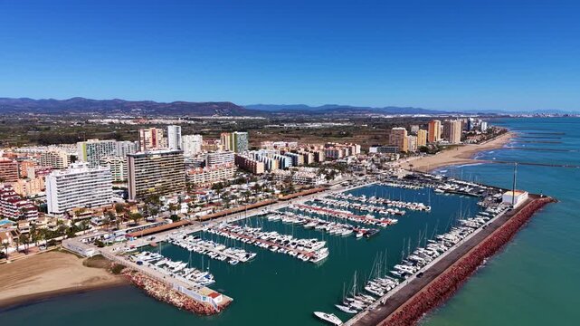 Pobla de Farnals marina and coastal town in Valencia, Spain, with sailboats docked, sandy beach, apartments, and mountain backdrop