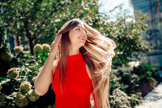 Happy woman in a red dress with long hair enjoying sunlight outdoors in an urban park