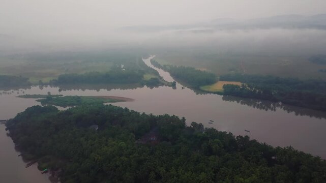 Ascending aerial view of misty Karli River wetlands with tree-covered islands in Konkan's Malvan Backwaters Tarkarli region, Maharashtra, India.