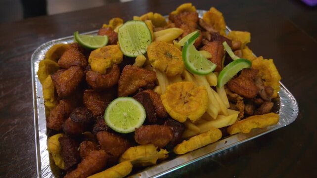 Cinematic high angle shot of a large platter of crispy Puerto Rican chicharr&oacute;n de pollo. Golden fried chicken chunks garnished with fresh lime slices in a local restaurant.