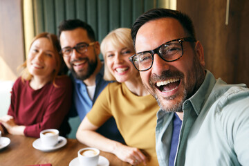 Obraz premium Group of happy friends smiling and laughing together while taking a selfie at a coffee shop