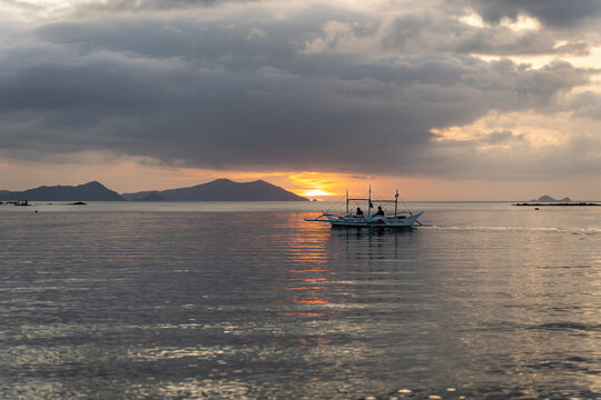 Solitary fishing boat sailing at sunset on calm water