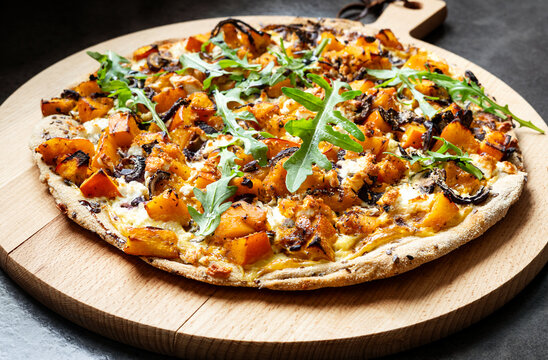 Homemade Hokkaido pumpkin pizza with arugula and balsamic glaze on wooden board