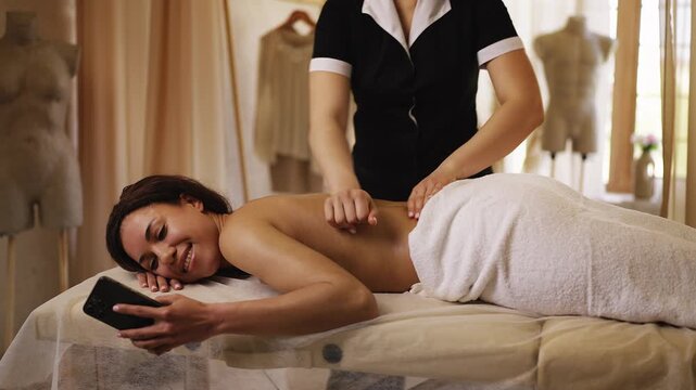 Smiling African American woman scrolling on cellphone during massage in spa