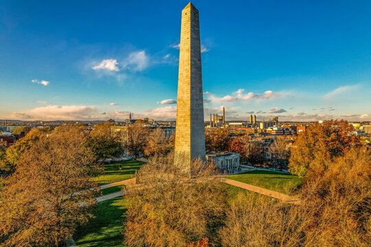 Aerial view of the majestic Bunker Hill Monument piercing the sky, the city sprawling beyond in a tapestry of autumnal hues, Boston, Massachusetts, United States.