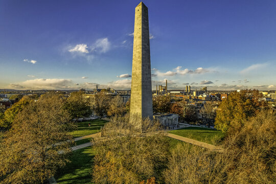 Aerial view of the Bunker Hill Monument rising above a park with fall foliage, contrasted against the distant city skyline, Boston, Massachusetts, United States.