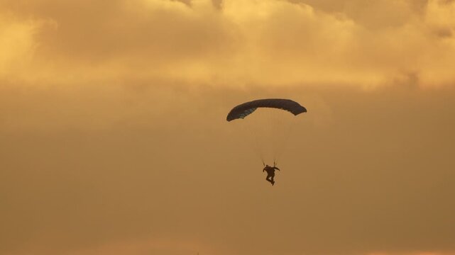 Paragliding skydiver sunset silhouette of paraglider descending through golden clouds at dusk