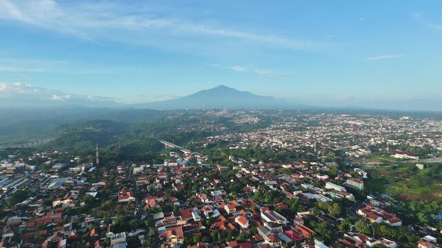 Aerial view of Yogyakarta city with Mount Merapi in the background under blue sky.