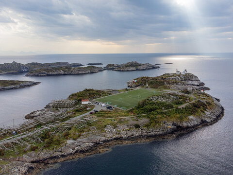 Aerial view of a football field on a rocky island, with the sun's rays reflecting off the water, Henningsvaer, Nordland, Norway.