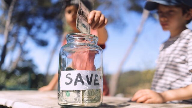 Young child placing dollar bills into a clear jar labeled save, learning financial responsibility and good money habits for future planning and independence
