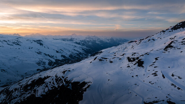Aerial view of a pristine, snow-blanketed mountain range under a pastel sky, the slopes bathed in the soft light of dawn, Val Thorens, Auvergne-Rhone-Alpes, France.