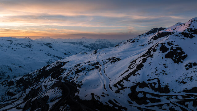 Aerial view of snow-capped mountains basking in the warm glow of the setting sun, the peaks casting long shadows across the serene landscape, Val Thorens, Auvergne-Rhone-Alpes, France.