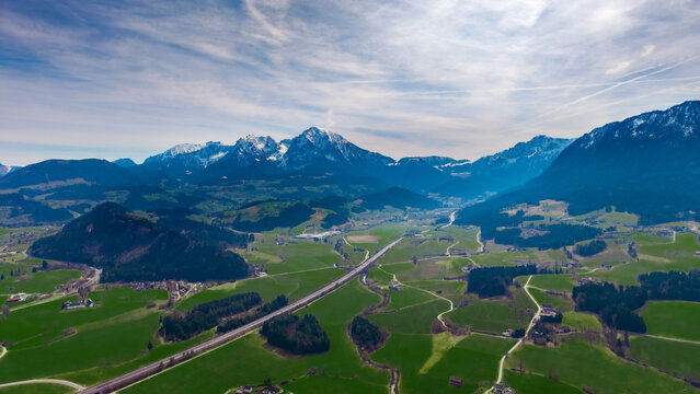 Aerial view of the vivid green Windischgarsten valley floor meeting rugged mountain peaks capped with snow under a vast, expansive sky, Windischgarsten, Upper Austria, Austria.