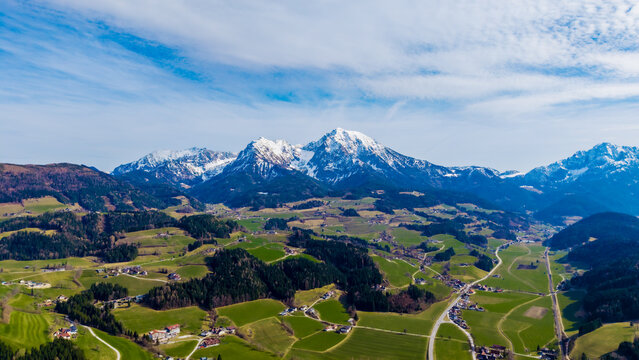 Aerial view of verdant fields contrasting with the snow-capped peaks under a bright sky, Windischgarsten, Upper Austria, Austria.