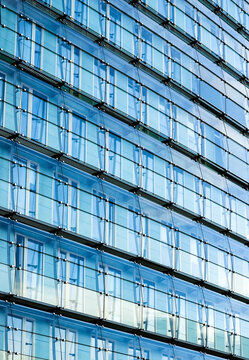 Blue glass facade of a modern building reflecting light and sky, showcasing contemporary architecture and clean geometric lines