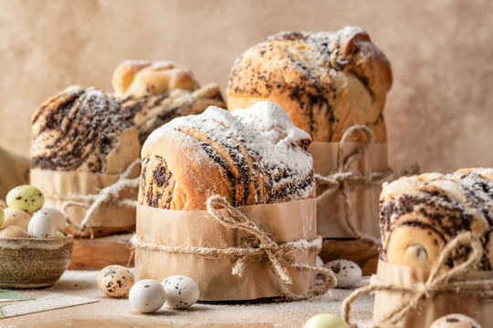 Easter cakes cruffins (Kulich) with poppy seed filling sprinkled with powdered sugar on beige textured background. Easter bread, easter eggs