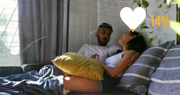Animation of financial data processing with heart icon over diverse couple embracing on sofa