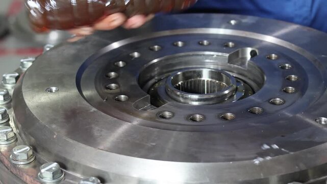 Mechanic pouring oil from a bottle to lubricate a bearing inside a heavy duty transmission housing during maintenance in a workshop.