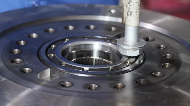 ​Mechanical technician installing a steel bearing into a heavy industrial metal component using a large hex bolt and hammer as manual tools inside a professional workshop.