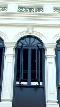 Close-up of elegant dark blue arched windows on a white historic building in Old Phuket Town, Thailand. Classic Sino-Portuguese architectural details, heritage shutters and colonial style facade.