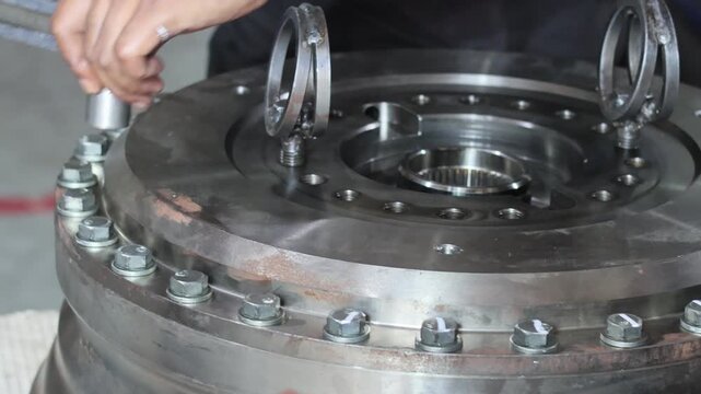 Technician tightening heavy machinery gear bolts using manual torque wrench tool in industrial workshop.