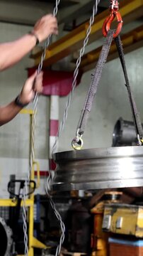 Technician lifting a heavy automatic transmission converter cover using a chain block and industrial hoist straps in a professional workshop.