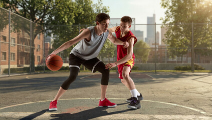 Obraz premium Two basketball players playing on outdoor court in city environment during match. Concept of street sports, urban lifestyle, fitness activity, youth culture, competitive play and outdoor training.