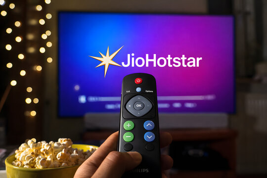Hand Holding TV Remote Streaming JioHotstar on Smart TV with Popcorn, Cozy Home Entertainment Night Scene