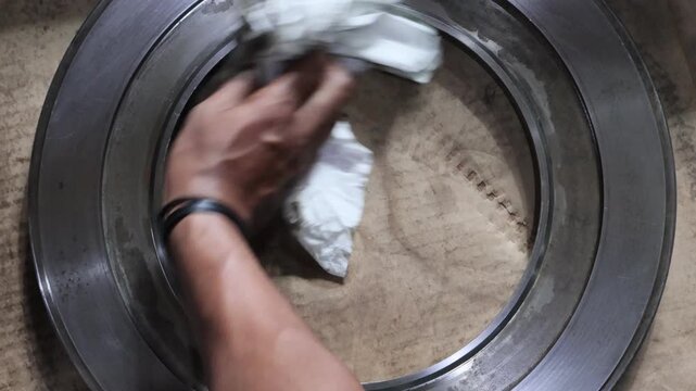 Close up of a mechanic hand cleaning a metal automatic transmission piston with a white cloth to remove oil and dirt during a maintenance process in a professional workshop.