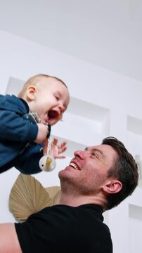 Loving Caucasian dad kissing his infant son. Man tosses the kid on one hand. Low angle view.
