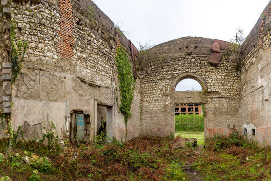 Interior of an abandoned Soviet era building in the ghost town of Tkuarchal. Crumbling stone and brick walls covered with ivy and moss under an open roof on a spring day. Abkhazia.