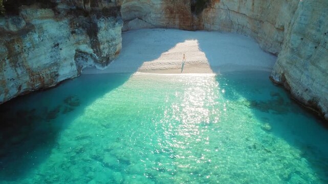 Woman walks on hidden rocky beach cove with turquoise water in summer Greece