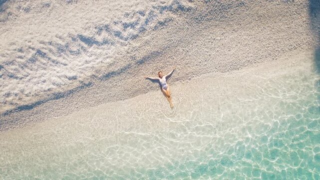 Woman relaxing where soft pebbles meet the clear shallow waters of the beach on greek Island