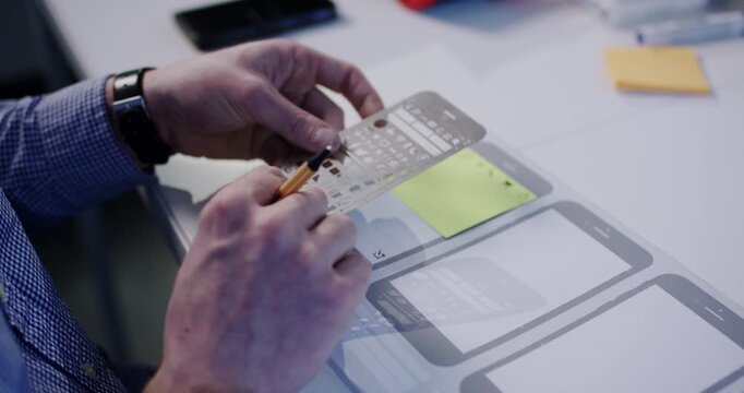 Close up of designer hands using metal stencil and pen to sketch mobile app wireframes on paper