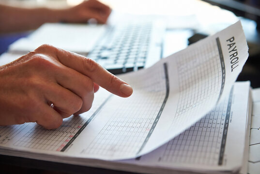 A person is reviewing a payroll document. It&rsquo;s happening at a desk, likely in an office environment.