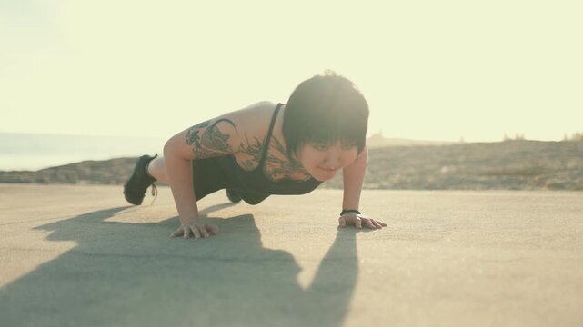 Tattooed asian woman performing push-ups during outdoor workout