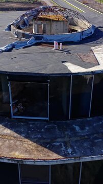 Aerial perspective of a flat roof with a circular opening and a metal dome frame. Top view of building roof with damaged dome structure. Vertical video.