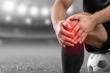 Obraz na płótnie Canvas Soccer player holding injured knee with red pain indicator, sitting on a soccer ball on grass.