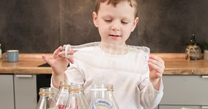 Curious boy studies empty bottle turning plastic container in hands. Preschooler inspects shape placing bottle back into sorting box after checking details
