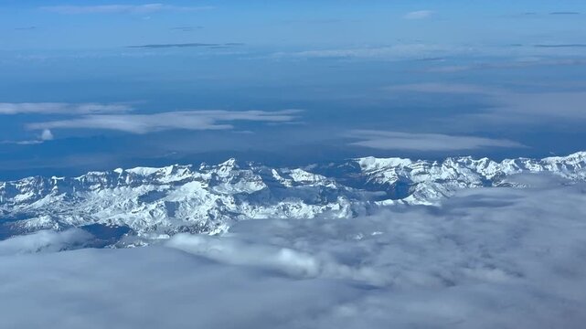 Elevated aerial view of the peaks of the snowed Pyrenees mountains emerging from a blanket of stratus clouds in a hazy sunny day. Cockpit view at 8000m high.