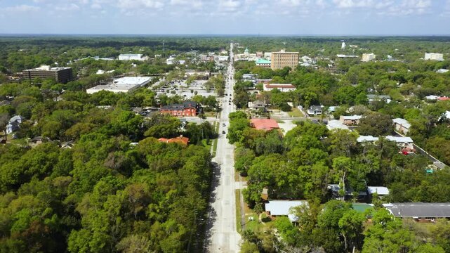 A wide aerial view reveals the small-town character of DeLand, Florida, framed by trees and a scenic downtown roadway.