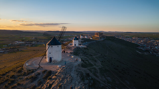 White windmills and Consuegra castle crown a golden La Mancha hilltop at sunset, evoking Don Quixote landscapes and offering sweeping panoramic views of rural Spain
