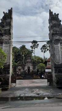 Bali Street Traffic in Front of Pura Dalem Ubud Temple, Motorbikes Passing Traditional Stone Gates and Palm Trees